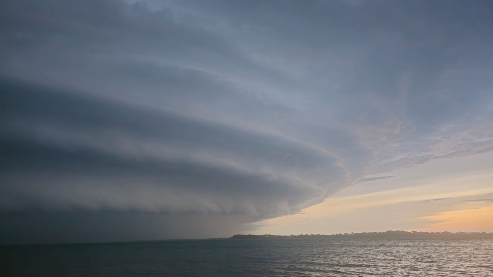 Nuage tubulaire roll cloud s'étirant à l'horizon sous un ciel orange au lever du soleil